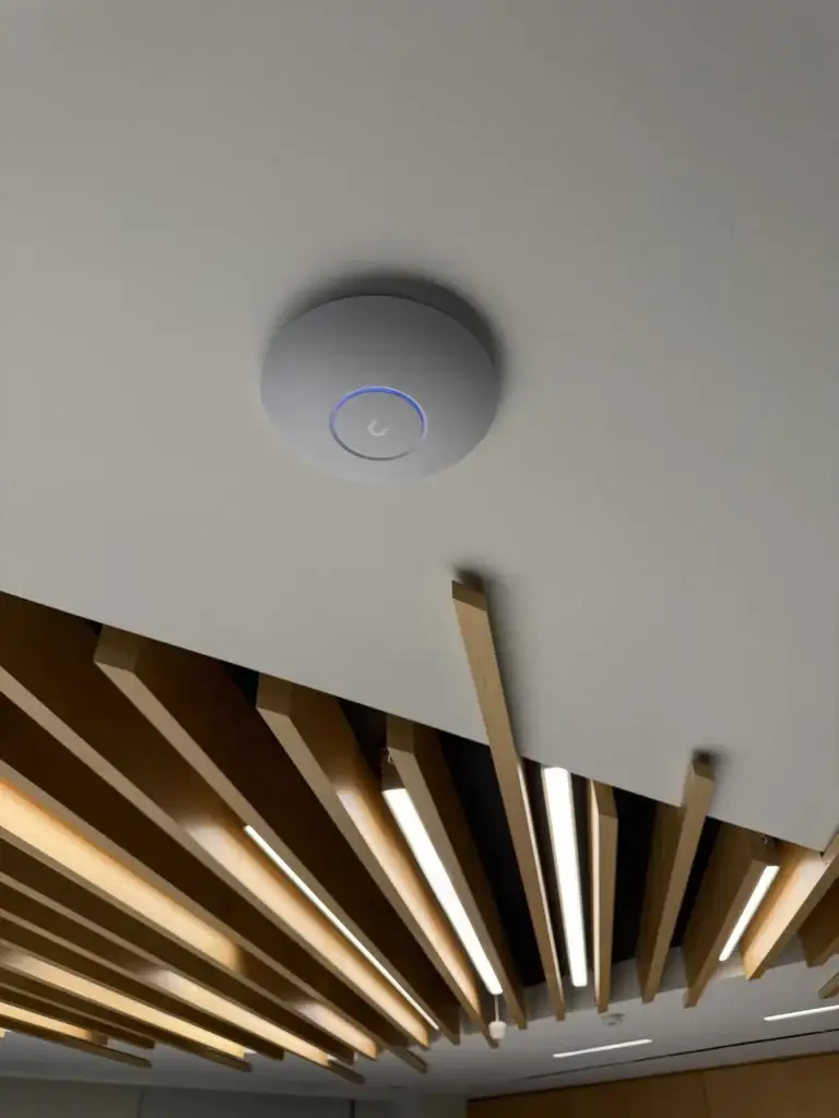 Cogency Global: From Dead Spots to Full-Office Wi-Fi 7 in One Week 3 UniFi Wi-Fi 7 access point mounted on a boardroom ceiling beside wood slat lighting